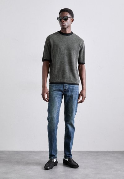 Maglione a maniche corte con texture di colore grigio scuro e bordo nero, abbinato a jeans blu. Gli occhiali da sole neri e le scarpe completano il look.