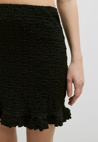 Zwarte smock mini-jurk met een gestructureerd, geraffineerd oppervlak en een afgeronde zoom. De stof heeft een zachte, elastische kwaliteit.