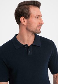 Polo shirt corto a maniche corte di colore blu scuro realizzato in tessuto texturizzato, con colletto classico e patta a due bottoni, dotato di polsini a coste.
