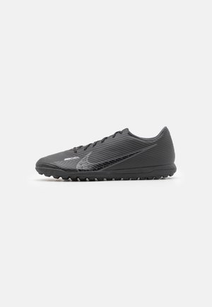 Chaussures de soccer noires avec une tige texturée, présentant des stries horizontales, une forme profilée et des crampons en caoutchouc pour l'adhérence.