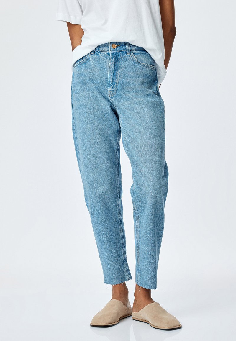 Ljusblå denimjeans med en avslappnad passform, med hög midja, fem fickor och fransade fållar. Bärs med beiga slip-on skor.
