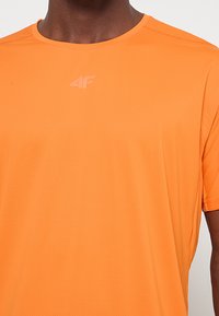 Pomarańczowy sportowy t-shirt wykonany z oddychającego materiału, z okrągłym dekoltem i krótkimi rękawami. Subtelne logo na wysokości klatki piersiowej.