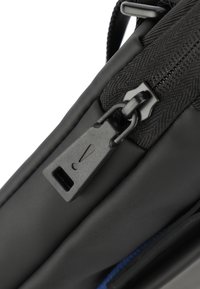 Borsa nera con zip caratterizzata da una superficie liscia opaca, in tessuto nylon, e un grande tirante della zip con un'etichetta, contrastata da una fodera blu.