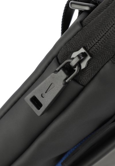 Sac zippé noir avec une texture mate lisse, en tissu nylon, et un grand tirette de fermeture éclair avec une étiquette, contrastant avec une doublure bleue.