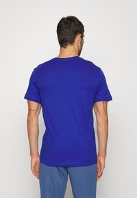 Niebieska koszulka z okrągłym dekoltem, wykonana z bawełny, z krótkimi rękawami i gładką fakturą. Tył jest jednolity, bez widocznych logo ani wzorów.