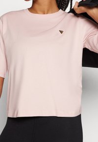 Rosa kortärmad t-shirt i mjukt tyg med rund halsringning och en liten triangulär logotyp på vänster bröst. Korta ärmar.