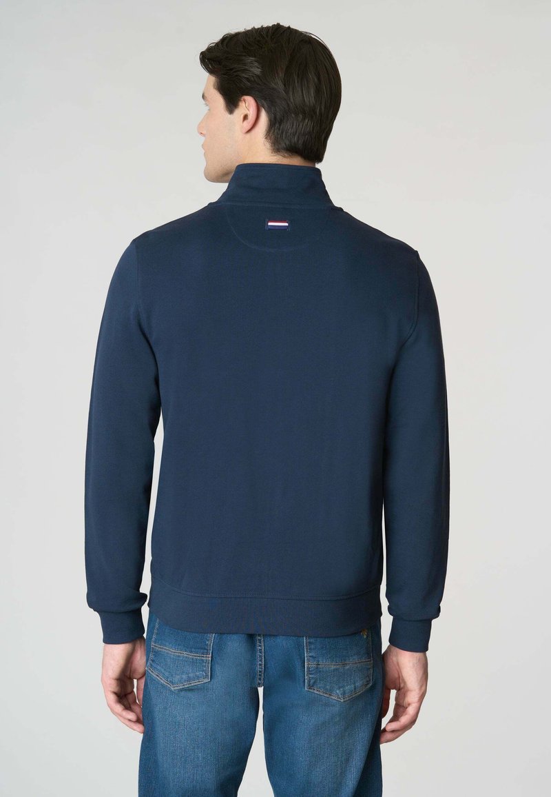 Marineblauer Pullover-Jacke mit hohem Kragen, gerippten Bündchen und Saum; verfügt über ein kleines Logopatch auf der Rückseite. Strukturiertes Strickgewebe.