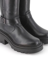 Botas de cuero negro hasta el muslo con una suela de plataforma gruesa, que presentan un detalle de correa con hebilla y una textura suave y pulida.