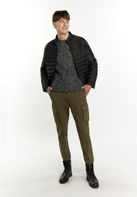 Jachetă pufosă neagră peste un pulover texturat gri, asortată cu pantaloni cargo de culoare verde măslin și bocanci negri cu șireturi.