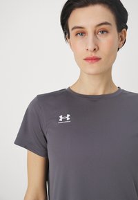 Hallgray sportlik särk, mis on valmistatud siledast kangast, ümmarguse kaelakaare ja lühikeste varrukatega. Vasakul rinnal on valge Under Armouri logo.