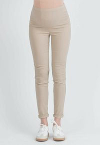 Beige hoge taillebroek met een slim fit, gemaakt van zachte, rekbare stof en met opgerolde manchetten, gecombineerd met witte sneakers.