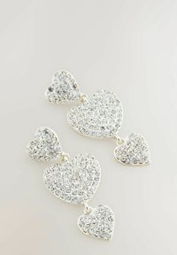 Silberfarbene hängende Ohrringe mit drei herzförmigen Anhängern, die mit klaren Strasssteinen verziert sind und in der Größe variieren, mit einem glatten Metallfinish.