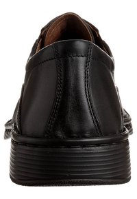Zapato de vestir de cuero negro visto desde atrás, que muestra las costuras cosidas, el cuello acolchado y la suela de goma estriada.