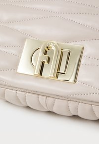Borsa in pelle beige chiaro con texture trapuntata, dotata di una chiusura in metallo dorato con il logo. I dettagli cuciti mettono in risalto il design.