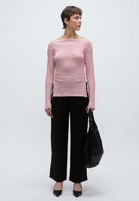 Világos rózsaszín és piros csíkos hosszú ujjú felső fekete, széles szárú nadrággal párosítva. A modell egy texturált fekete táskát hord, hegyesorrú fekete cipőben.