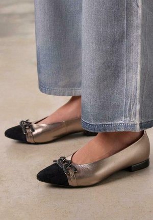 Flats en bronze métallique et noir avec un bout pointu, dotés d'une petite boucle décorative et d'un petit talon, associés à un denim clair.