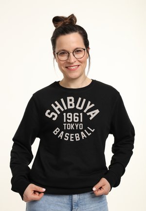 Felpa nera con la scritta "SHIBUYA 1961 TOKYO BASEBALL" stampata in grigio chiaro. Caratterizzata da maniche lunghe e scollatura rotonda. Vestibilità casual e texture del tessuto.