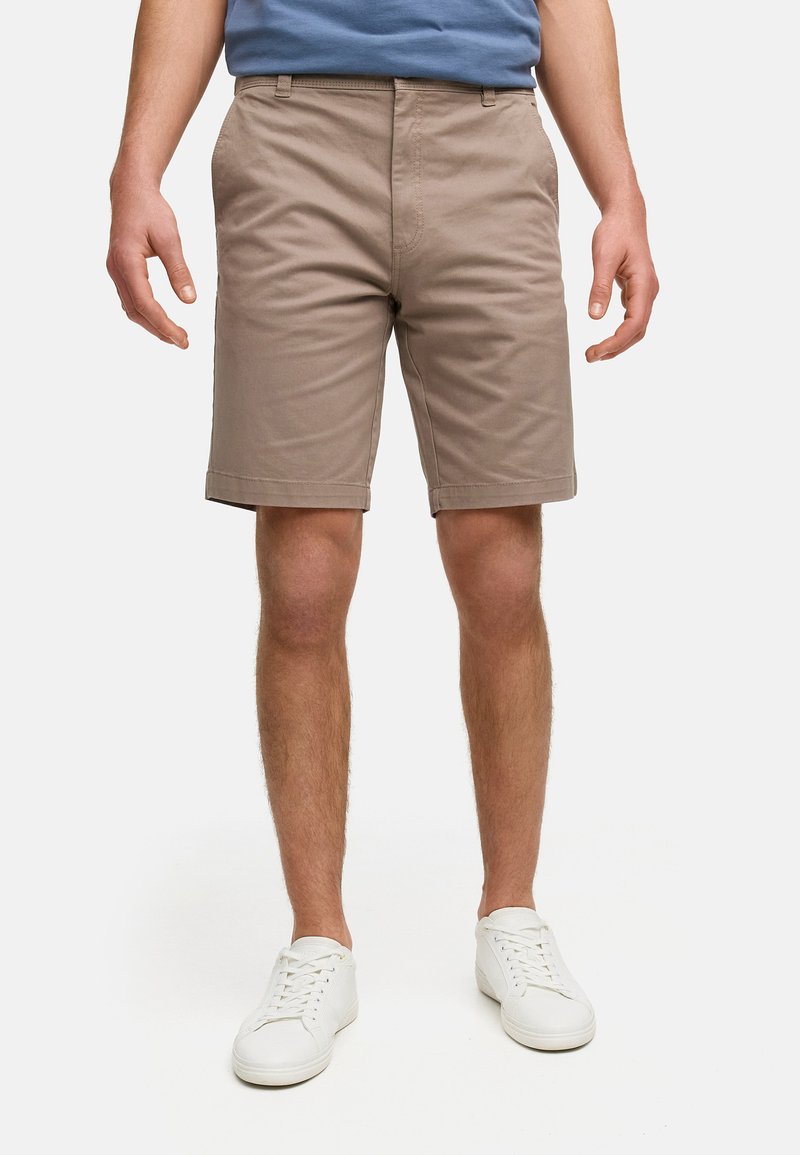 Shorts en coton marron avec un devant plat, des poches et un ourlet retourné. Assortis à des baskets blanches et un t-shirt bleu.