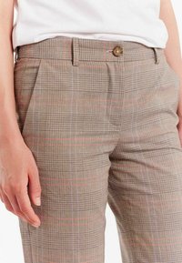 Pantalons à carreaux bruns en tissu texturé, avec de fines lignes rouges et bleues, une taille standard et une fermeture à bouton unique.