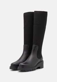 Bottes noires montantes en cuir lisse pour la partie inférieure et en tissu texturé doux pour la partie supérieure. Dotées d'une semelle plateforme épaisse.
