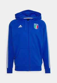 Veste à capuche bleue zippée en tissu doux, avec des rayures blanches sur les manches et un logo de drapeau italien sur la poitrine. Deux poches avant.