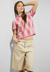 Růžový a béžový argyle vzorovaný pletený svetřík s krátkým rukávem a zkráceným lemem, který je kombinován se světle béžovými šortkami s přední kapsou.