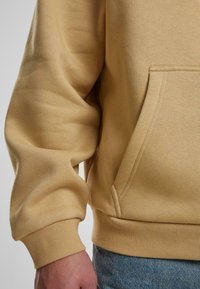 Gelber Sweatshirt aus weichem Stoff, mit Kängurutasche, gerippten Bündchen und Saum, glatter Textur und lockerem Sitz.