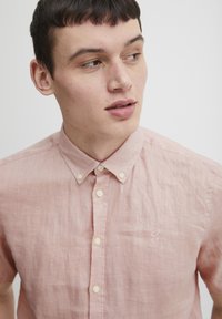 Korte mouwen, lichtroze linnen shirt met een button-up kraag en een klein geborduurd logo op de linkerborst, met crèmekleurige knopen.