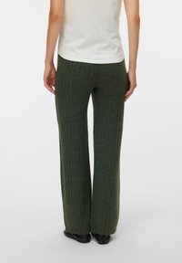 Green ribbed knit pants with a flared leg design, featuring a soft texture and a high waistband, paired with black shoes.