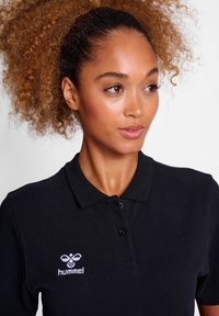 Czarna koszulka polo z fakturowanej tkaniny, z kołnierzykiem, wyposażona w zapięcie na trzy guziki oraz białym haftem logo "hummel" na piersi.