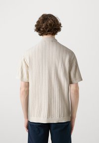 Koszulka polo z krótkim rękawem w jasnobeżowym kolorze, ozdobiona fakturowanym wzorem jodełki oraz kontrastującym kołnierzem i mankietami.