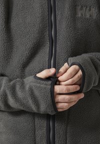Grijze fleece jack met een textuur oppervlak, ritssluiting aan de voorkant en contrasterende zwarte afwerking. Heeft aansluitende mouwen en een logo detail op de borst.