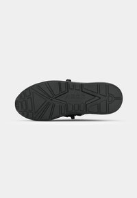 Black rubber shoe sole with textured tread pattern, featuring logo "ARKK" and various angular designs for traction.