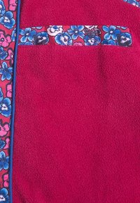 Ljust rosa fleece tyg med blommönster i blått, rosa och vitt längs kanten och öppningen till fickan.