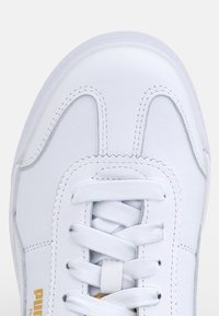 Baskets blanches avec une tige en cuir lisse, un bout arrondi, des détails cousus et des lacets plats. Comprend un accent logo doré sur le côté.