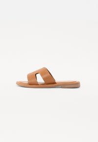 Braune Leder-Slide-Sandale mit flacher Sohle, ausgestattet mit einem breiten Riemen mit Ausschnitt und einer glatten Textur. Einfaches und minimalistisches Design.