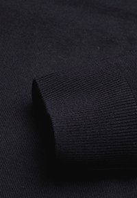 Dunkelblau gestrickter Pullover im Detail, mit einem gerippten Bündchen und glatter Textur, der das taillierte Design und das gleichmäßige Stoffmuster betont.