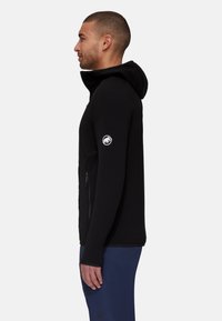 Black fleece jacket with a hood, zippered front pocket, and logo patch on the left sleeve. Smooth texture and fitted design.