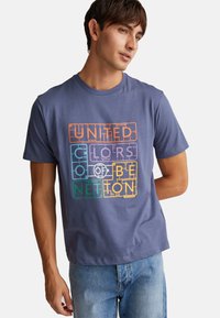 Camiseta de algodón azul de manga corta con un diseño gráfico de texto multicolor "UNITED COLORS OF BENETTON" en el frente. Ajuste casual.