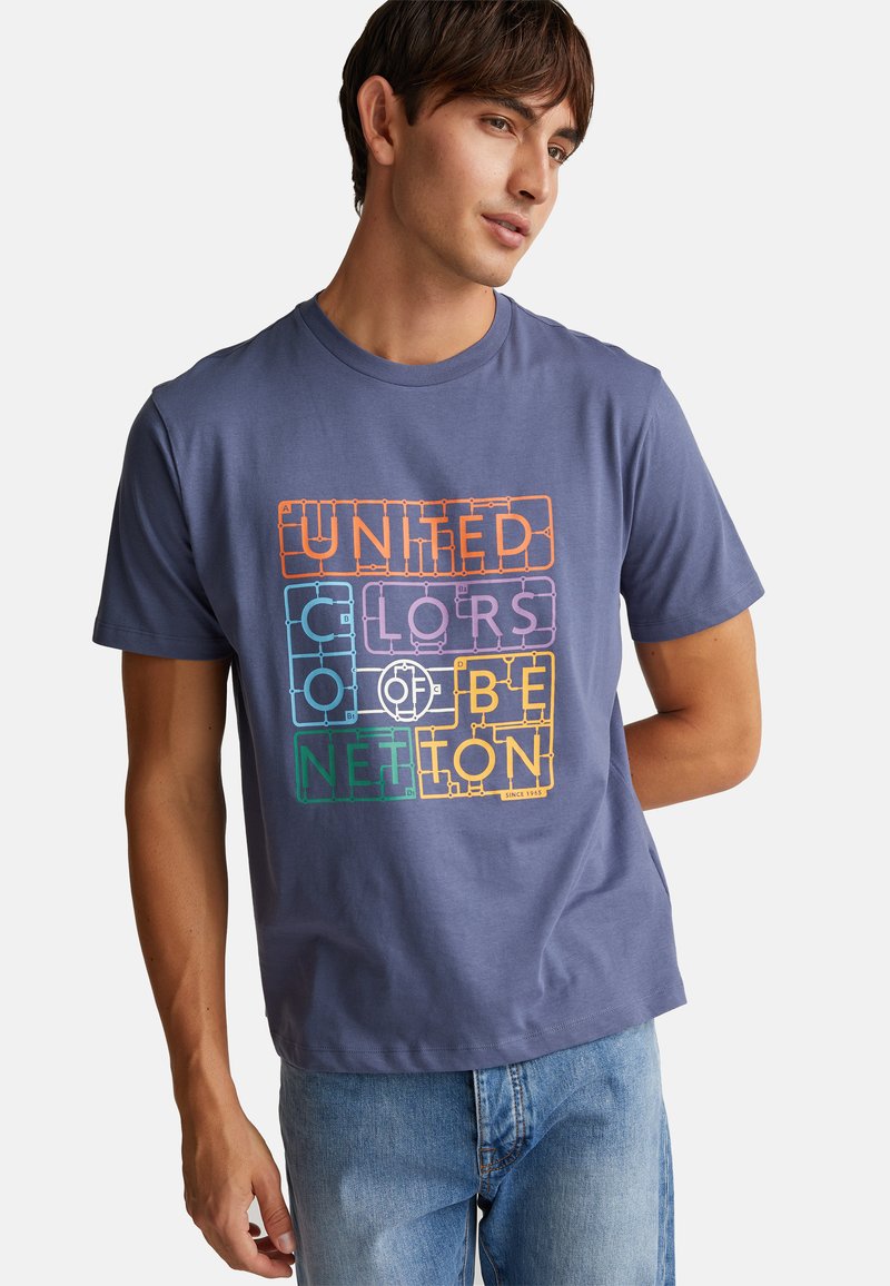 Camiseta de algodón azul de manga corta con un diseño gráfico de texto multicolor "UNITED COLORS OF BENETTON" en el frente. Ajuste casual.