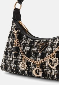 Tote tas in zwart-wit tweed met een gouden ketting en decoratieve bedels. Voorzien van een opvallend logo en een ritssluiting.