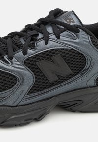 Zwarte sportieve schoen met een mesh bovenstuk en textuuraccenten, voorzien van een opvallend zwart "N"-logo en zwarte veters.