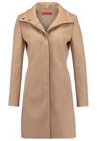 Beige jas met een geknipte kraag, enkele drukknoopsluiting en zwarte piping. Voorzien van twee zijzakken en decoratieve versieringen bij de kraag.