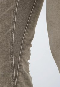 Pantalones caqui de corte ajustado, con fina textura de rombos en diagonal y costuras en crema contrastantes a lo largo de la costura lateral.