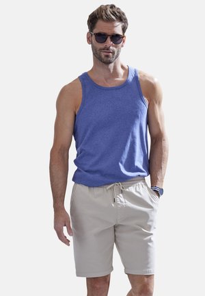 Blaues Baumwoll-Tanktop mit Rundhalsausschnitt, kombiniert mit hellbeigen Shorts mit Kordelzug. Beinhaltet dunkle Sonnenbrille und eine Armbanduhr.
