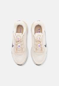 Zapatillas deportivas beige con parte superior de malla técnica, acentos morados y suela negra. Cuentan con cierre de cordones y collar acolchado para mayor comodidad.