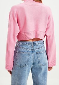 Korte roze gebreide trui met een hoge hals en ribbelrand, gecombineerd met hooggerokte lichtblauwe spijkerbroeken met achterzakken.