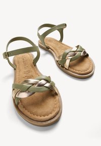 Sandali intrecciati verdi e dorati con cinturini in pelle sintetica, soletta imbottita color beige e suola in gomma texturizzata. Inclusa una cinghia regolabile alla caviglia.