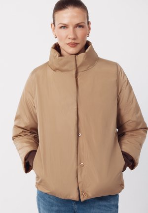 Jasnobrązowa pikowana kurtka z wysokim kołnierzem, guzikami z przodu i bocznymi kieszeniami. Charakteryzuje się gładką, błyszczącą teksturą i luźnym krojem.