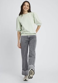 Pull léger vert, texturé, avec des manches bouffantes, associé à un jean gris taille haute à jambe large. Modèle portant des baskets crème.